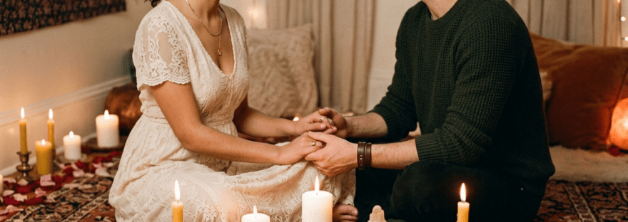 Couple holding hands seated on rug with candles, rose petals, and crystals