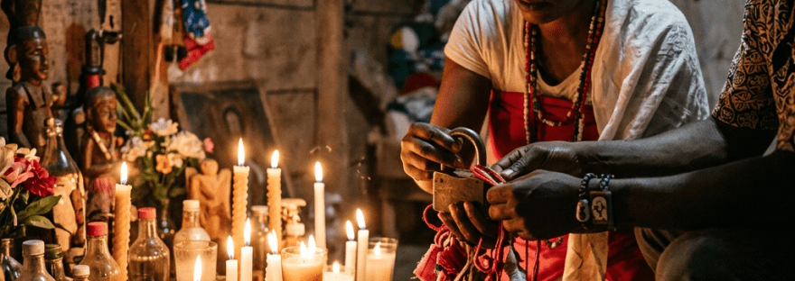 Two individuals engaged in a ritual with candles, bottles, and fabric in a wooden room