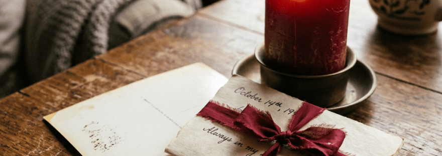Handwritten letter with red ribbon and red candle on wooden table
