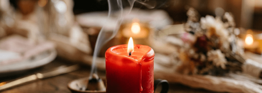 Red candle burning on rustic wooden table next to two wedding rings and dried flowers
