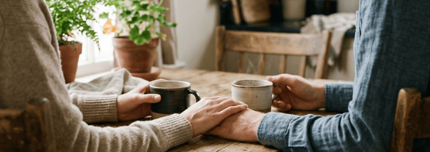 Couple holding hands over coffee at a sunlit kitchen table